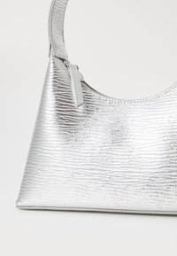Sac à main argenté avec une finition métallique texturée. Présente une forme semi-circulaire et une anse fine. Fermeture avec un petit détail de tag.