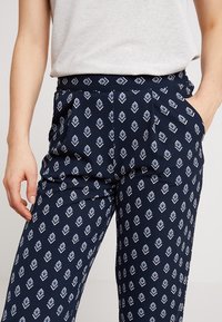 Granatowe spodnie w wzór diamentu w kolorze białym i niebieskim. Posiadają kieszenie i wygodny pas. Wykonane z lekkiego materiału.