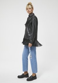 Czarna skórzana kurtka z frędzlami, w połączeniu z jasnoniebieskimi spodniami dżinsowymi w stylu distressed oraz czarnymi loafersami. Gładka tekstura, projekt z kołnierzykiem.