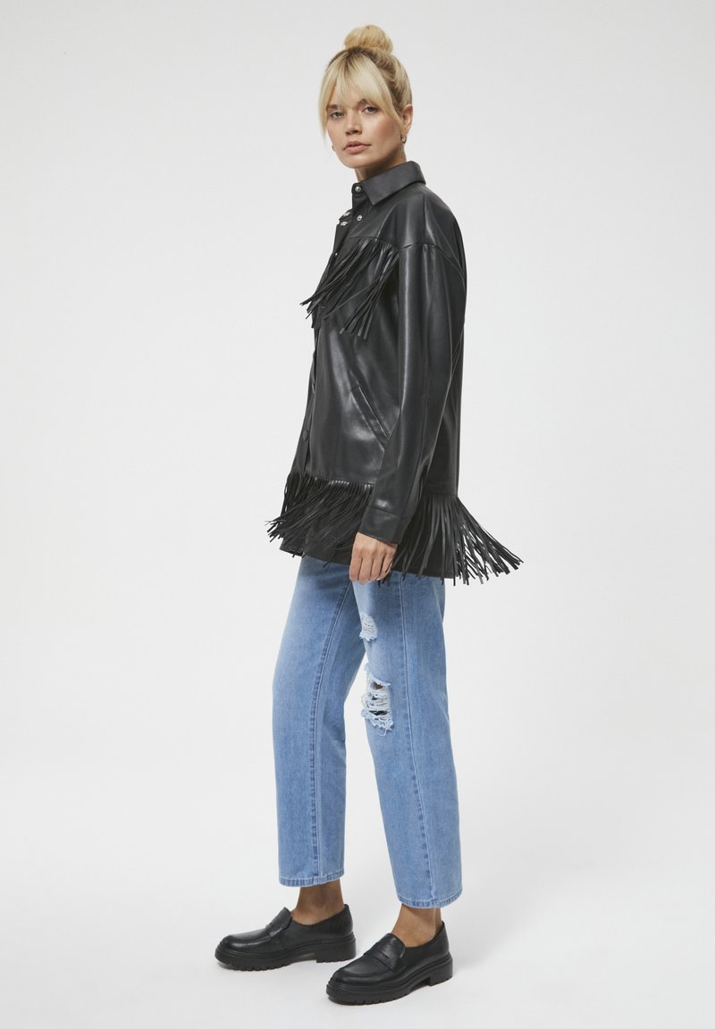 Czarna skórzana kurtka z frędzlami, w połączeniu z jasnoniebieskimi spodniami dżinsowymi w stylu distressed oraz czarnymi loafersami. Gładka tekstura, projekt z kołnierzykiem.