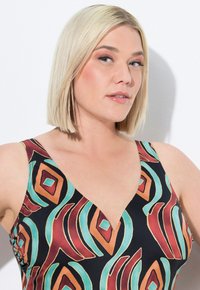 Débardeur noir avec un motif abstrait coloré comprenant des formes rouges, orange, teal et crème ; décolleté en V et bretelles larges.