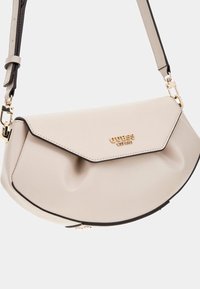 Borsa a tracolla beige con forma curva, texture liscia e hardware dorato. Presenta una chiusura a pattina con logo del marchio e dettagli neri.