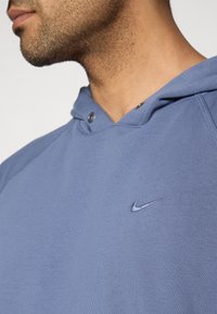 Sweat à capuche Nike bleu clair en tissu texturé, avec une capuche à cordon de serrage et un petit logo brodé sur la poitrine.
