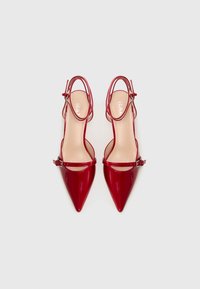 Red patent leather slingback heels with pointed toe, ankle strap, and buckle detail. Smooth texture with a shiny finish.
