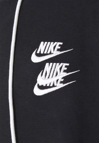 Svart tyg med vita, broderade Nike-logotyper i ett återkommande mönster. Slät textur med kontrasterande vita sömmar.