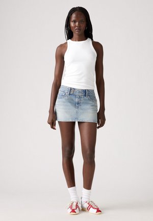Lichtblauwe denim minirok met een aansluitende taille, voorzien van een vijfknops sluiting en subtiele vervaging. Gecombineerd met een witte geribde tanktop en sneakers met rode accenten.