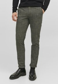 Pantalons à carreaux verts avec une coupe slim, avec une texture subtile. Associés à des mocassins en cuir noir.