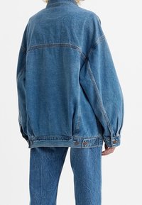 Ljusblå denimjacka med avslappnad passform, stora ärmar och knapprygg på manschetterna. Strukturerad yta med söm på bakstycket.