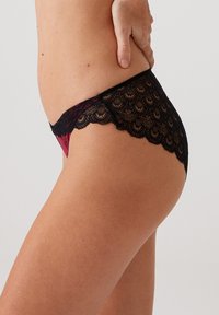 Lace string met een gegolfde zwarte kanten rand en een doorschijnend rood lijfje. Het ontwerp benadrukt ingewikkelde kanten patronen met een gladde afwerking.