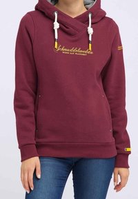 Sudadera burdeos con cuello cruzado, cordones blancos y detalles amarillos. Presenta bolsillos laterales y un logo bordado. Textura suave.