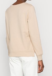 Felpa beige con scollo arrotondato e maniche lunghe, caratterizzata da orlo e polsini a costine, realizzata in morbido tessuto misto cotone.