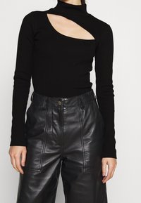 Svart långärmad topp med hög krage och en asymmetrisk utskärning, i kombination med högmidjade läderbyxor med sidofickor.