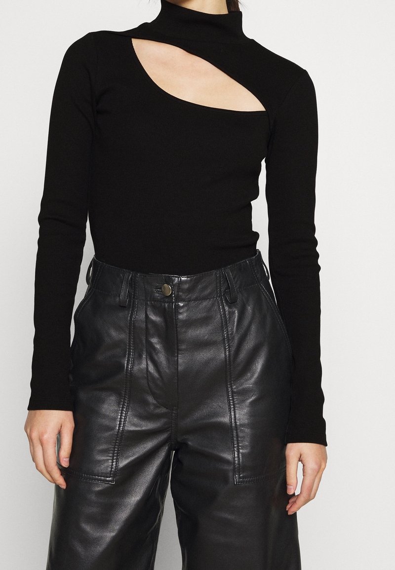 Svart långärmad topp med hög krage och en asymmetrisk utskärning, i kombination med högmidjade läderbyxor med sidofickor.