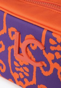 Bolsa de tela morada con un patrón abstracto naranja, que presenta un logo texturizado en naranja con la inscripción "LOLA CASADEMUNT" contra la superficie.