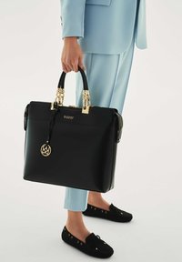 Fekete bőr kézitáska arany díszítésekkel, két felső fogantyúval és logó medállal. Cipzáras záródással és struktúrált, téglalap alakú formával rendelkezik.