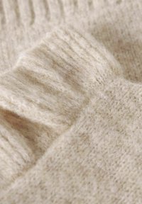 Béžová vlněná pletenina s měkkým, texturovaným povrchem a ribbovanými akcenty, zobrazující teplé, neutrální tóny při detailním pohledu.