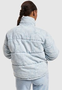 Chaqueta de plumas azul claro con tejido estampado, cuello alto y diseño acolchado. Textura suave y ajuste holgado, con una parte trasera redondeada.