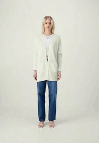 Svetlozeleni kardigan na otvoreno s teksturiranim pletenim vzorcem, dolgi rokavi in stranske žepe, v kombinaciji z modrimi hlačami visoke pasu.