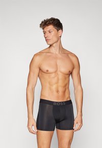 Black boxer briefs with a thick waistband featuring the brand logo "BOSS." The fabric appears smooth with a fitted design and mid-thigh length.