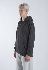 Sweatshirt à capuche gris foncé avec une poche avant, un col à cordon et des poignets côtelés, associé à un jean clair et ample.