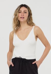 Canotta bianca a costine con scollatura a V profonda e spalline sottili, abbinata a pantaloni neri larghi con coulisse. Tessuto liscio, silhouette aderente.