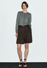 Chemise boutonnée à manches longues grise associée à un short taille haute marron et des sandales noires. La tenue comprend une ceinture noire tressée.