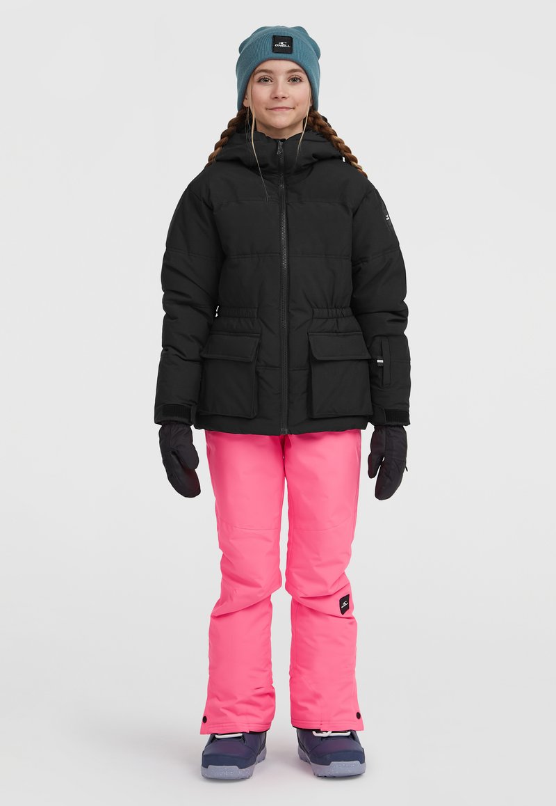 Černá péřová bunda se dvěma předními kapsami, doplněná jasně růžovými snowboardovými kalhotami. Tmavě modré boty a tyrkysová čepice dotvářejí celkový vzhled.