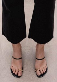 Zwarte platte sandalen hebben een minimalistisch ontwerp met een gouden accenten. De zool is glad en de straps zijn dun en ingetogen.