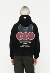 Zwarte hoodie met een grote grafische afbeelding op de achterkant met gele en bordeauxrode accenten. Text leest "POP'S RECORD STORE, BEALE STREET, MEMPHIS, TENNESSEE."