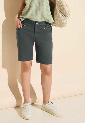 Shorts gris en tissu lisse, avec deux poches avant et une coupe ajustée. Associés à un haut vert texturé et des baskets blanches.
