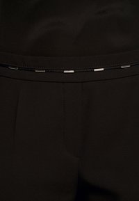 Černé kalhoty na míru s hladkou strukturou, zdobené stříbrným akcentem na pase a jemným řasením.