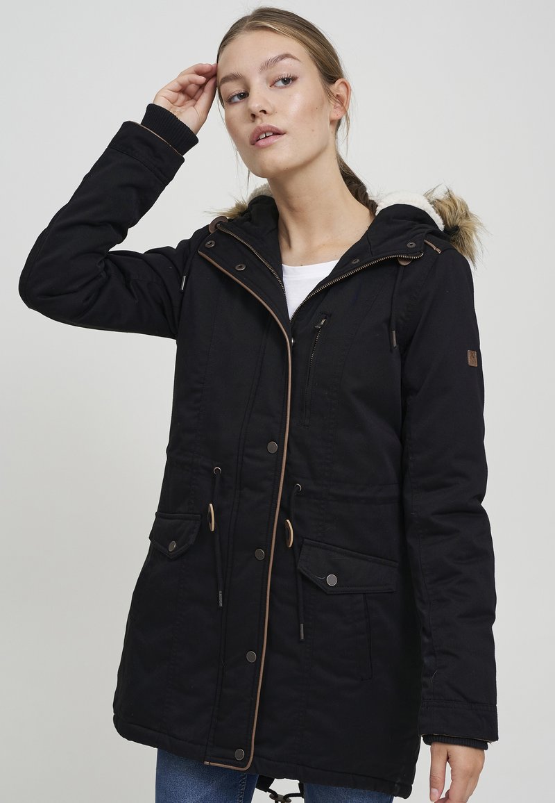 Black parka coat with a fur-lined hood, adjustable drawstrings, zip and snap closures, and dual front pockets. Features brown accents.