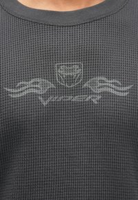 Sötétszürke, texturált pulóver gofrumos kötésmintával, finom nyomott logóval és lángdíszítéssel a mellkason.