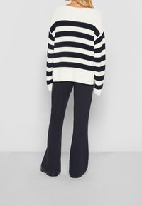 Maglione a maglia con strisce orizzontali blu navy e bianche, scollo ampio, spalle scese, abbinato a pantaloni svasati blu navy e scarpe nere.