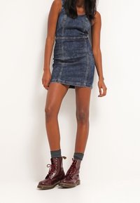 Jeansklänning i mörkblått med figursydd design och sömdetaljer. Burgundy snörda kängor och grå strumpor kompletterar looken.