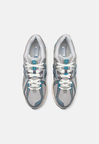 Pár šedých a modrých běžeckých bot New Balance 1906 s bílými tkaničkami, pohled zeshora na bílém pozadí.