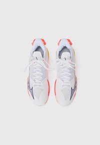 Weiße Sportschuhe mit grauen Akzenten, Mesh-Bereichen und roten Highlights an den Fersen und Sohlen. Sie besitzen weiße Schnürsenkel und einen gepolsterten Kragen.