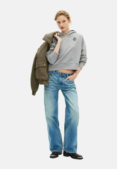 Felpa grigia corta con logo, giacca esterna a scacchi, jeans a gamba larga di colore azzurro chiaro e stivali neri con dettagli in argento, su sfondo bianco.