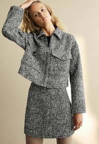 Veste en tweed noir et blanc avec deux poches avant et une fermeture éclair, associée à une jupe assortie. Tissu à texture lisse.