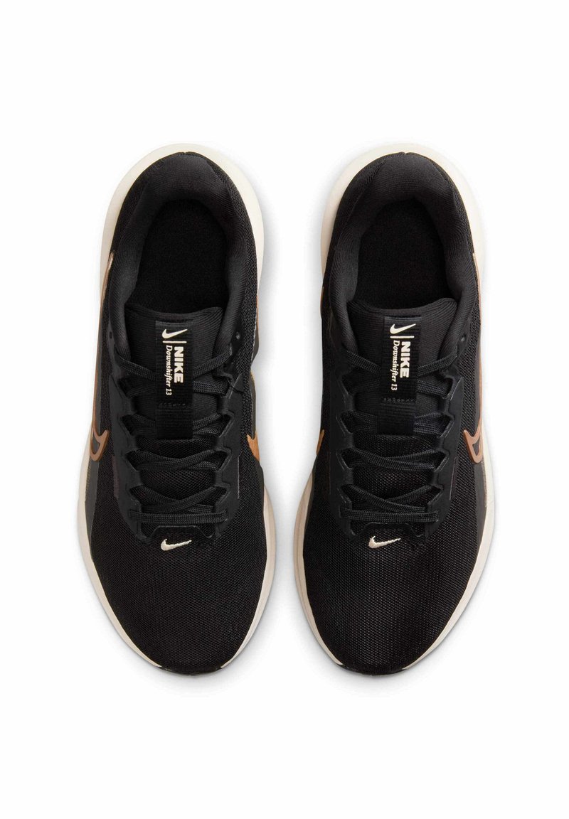 Zwarte sportschoenen met een bovenwerk van mesh, voorzien van een beige swoosh-logo en een witte zool. De veters en tong zijn ook zwart en tonen het merkembleem.