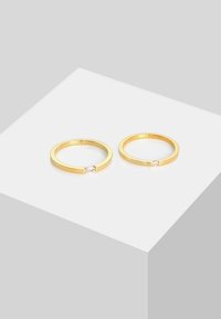 Guld ringe med et minimalistisk design og en glat overflade. Hver af dem har en lille, klar sten indsat i banden.