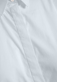 Light blue button-up shirt made of smooth fabric, featuring a pointed collar, single button closure, and subtle textured surface.