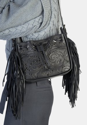 Borsa nera in pelle con complesso motivo a spirale borchiato, bordi sfrangiati e chiusura a coulisse. Indossata su maglione e pantaloni grigi.