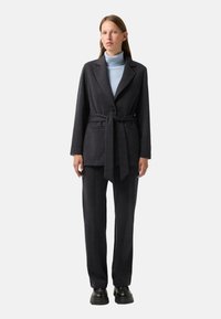 Blazer ajusté gris foncé avec une ceinture, associé à un pantalon ample assorti et un col roulé bleu clair. Tissu lisse avec un design structuré.