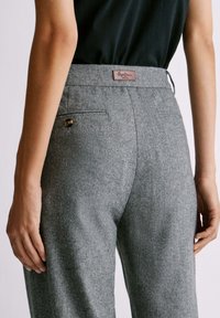 Pantalones de espiga grises con un corte entallado, que presentan una etiqueta marrón en la cinturilla y un bolsillo trasero con detalle de botón.