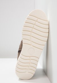Chaussure en daim marron avec une semelle en caoutchouc blanche, présentant un motif de bande de roulement texturé et un petit détail de fermeture éclair sur le côté.