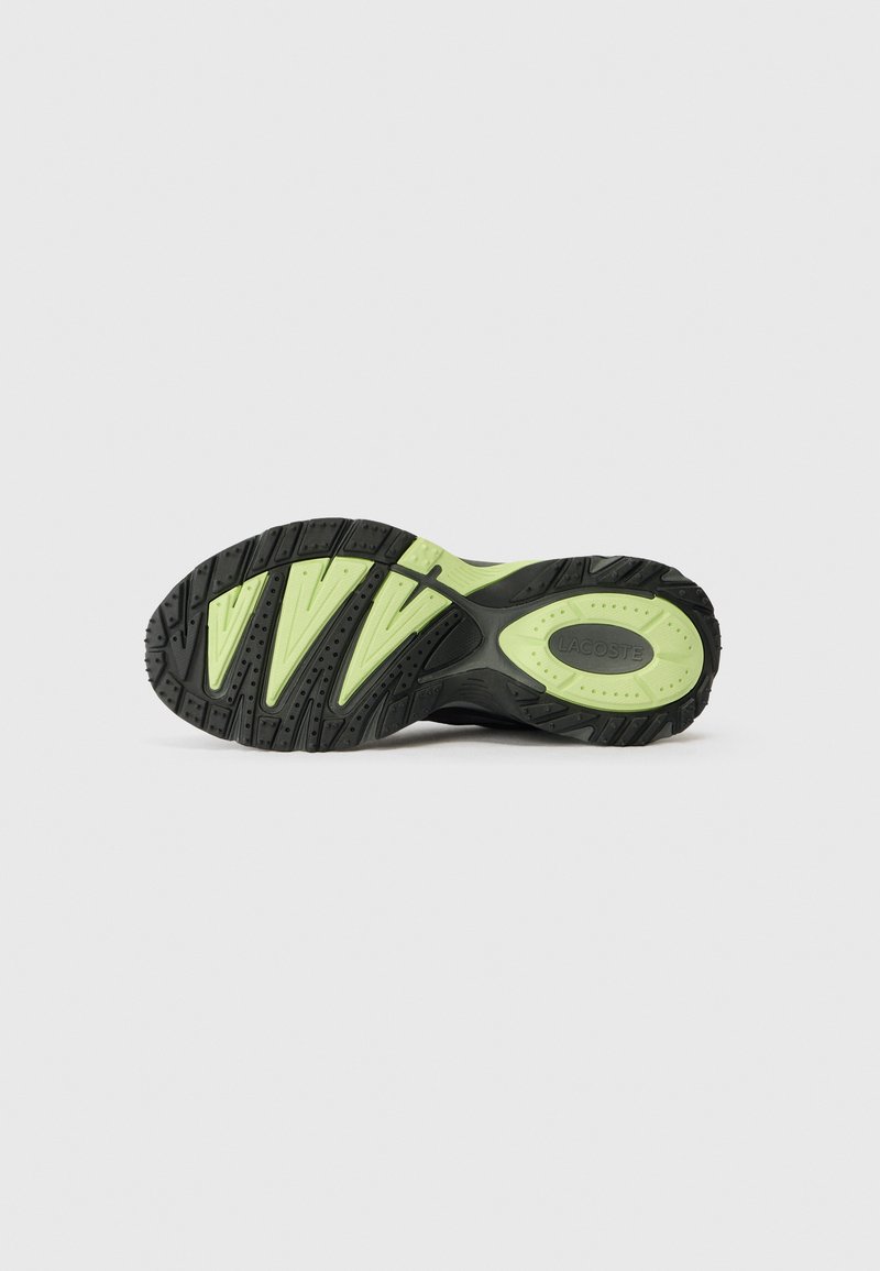 Black and light green Lacoste shoe sole with deep treads and logo visible on the heel area, isolated on a plain background.
