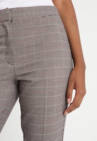 Byxor i ett brunt och krämfärgat hundtandsmönster, skräddarsydd passform, med en mjuk textur och framfickor, visade från midjan och ner.