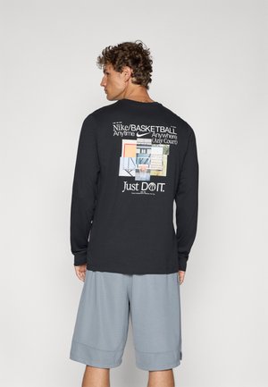 Black long-sleeve shirt with graphic design featuring basketball court imagery and "Just Do It" text. Worn with grey shorts.