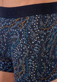 Boxers gemaakt van rekbare katoen met een marineblauwe achtergrond, voorzien van bloemenpatronen in lichtblauw, oranje en wit. Elastische tailleband met de opdruk "HOM."